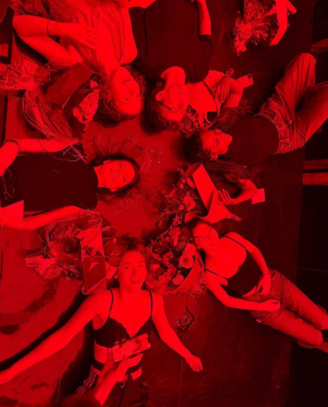The cast lying in a circle in red light
