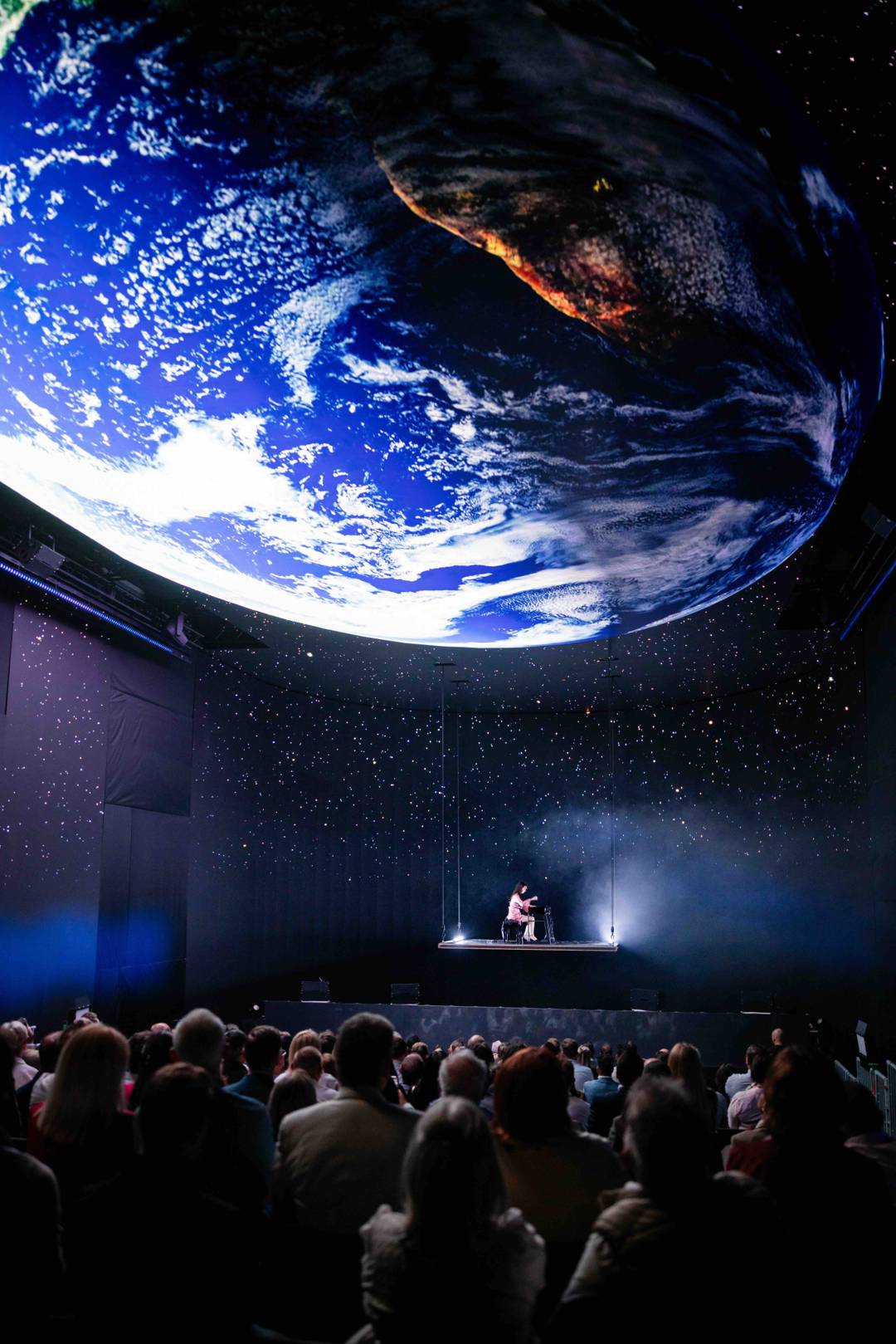 The audience in front of the stage, under a giant Earth on the LED ceiling